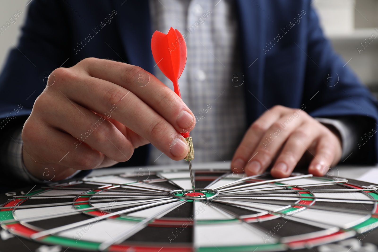 Photo of Business targeting concept. Man with dart aiming at dartboard at table, closeup