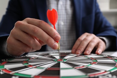 Business targeting concept. Man with dart aiming at dartboard at table, closeup