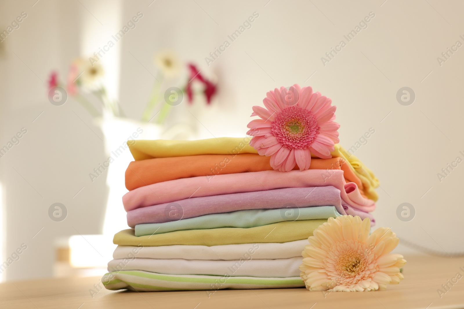 Photo of Stack of clean clothes and flowers on wooden table