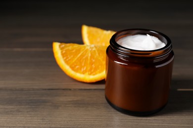 Photo of Jar of face cream and orange slices on wooden table, space for text
