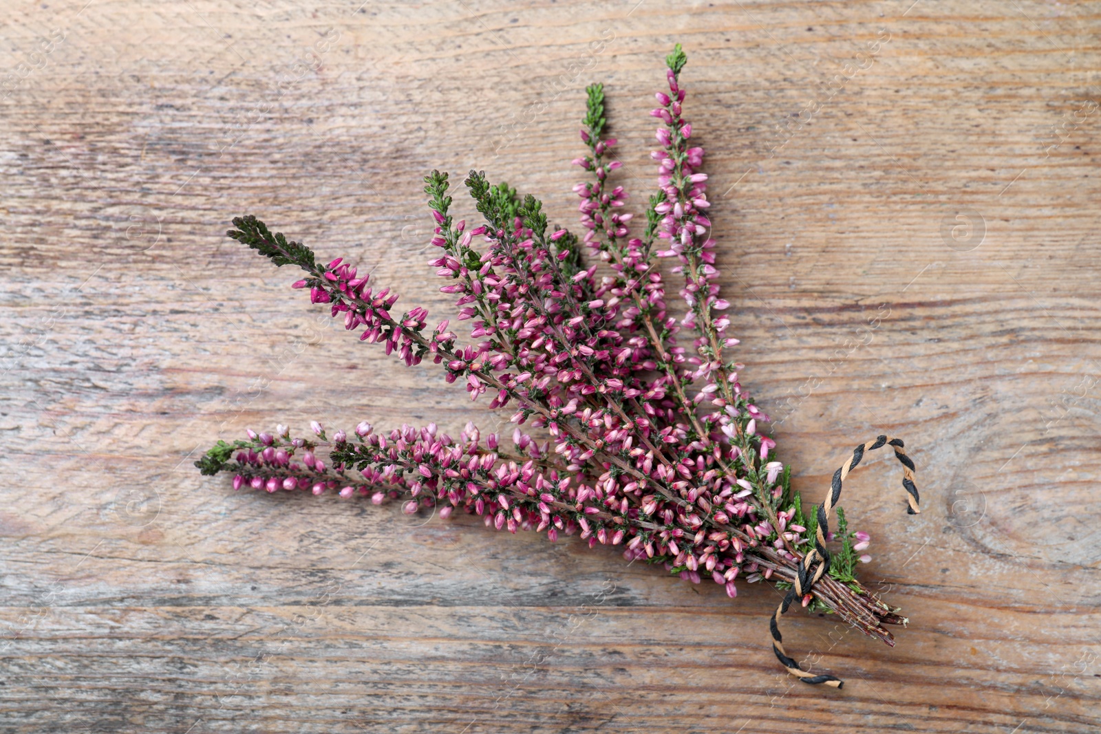 Photo of Bunch of heather branches with beautiful flowers on wooden table, top view