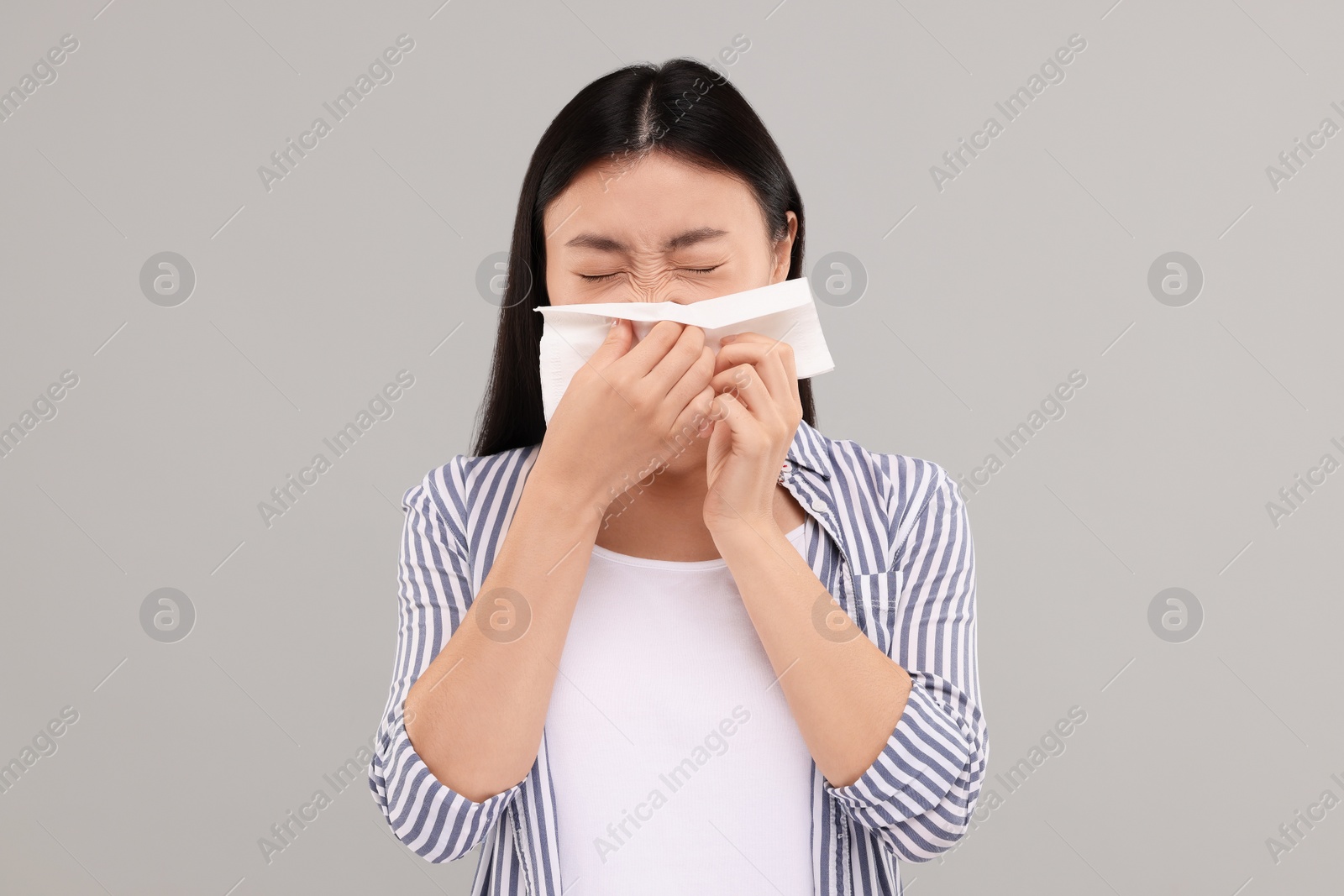 Photo of Suffering from allergy. Young woman with tissue sneezing on grey background