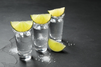 Photo of Mexican Tequila shots, lime slices and salt on black table