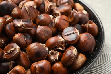 Delicious roasted edible chestnuts in frying pan on table, closeup