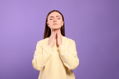 Young woman with sore throat on violet background