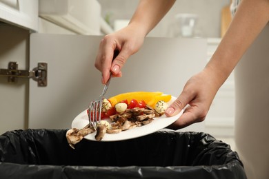 Woman throwing vegetable and mushrooms into bin indoors, closeup