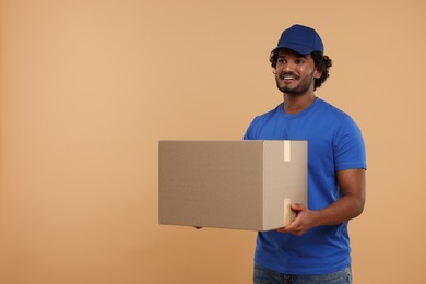 Photo of Happy young courier with parcel on light brown background, space for text