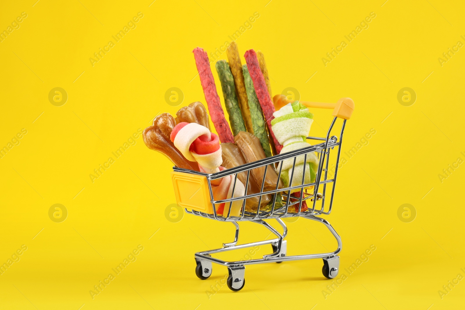 Photo of Small shopping cart with different pet goods on yellow background. Shop assortment