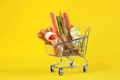 Small shopping cart with different pet goods on yellow background. Shop assortment