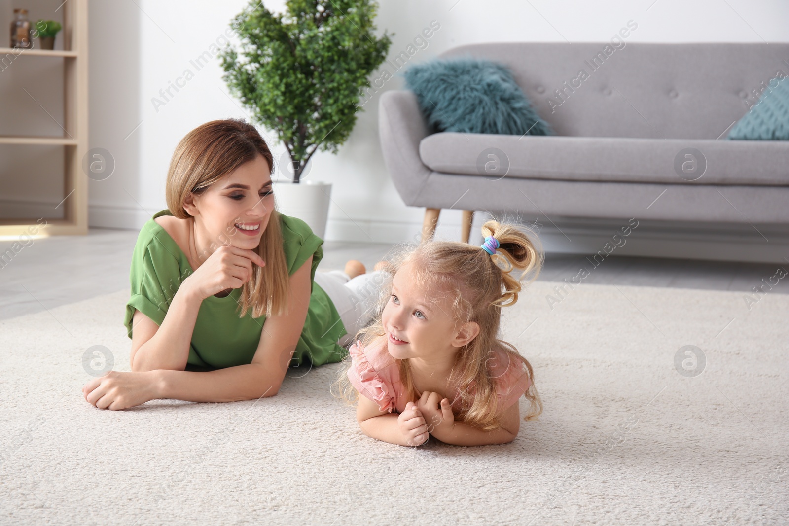 Photo of Cute little girl and her mother lying on cozy carpet at home