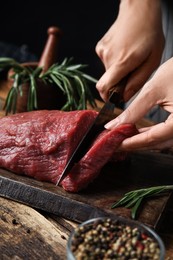 Woman cutting fresh raw meat at wooden table, closeup