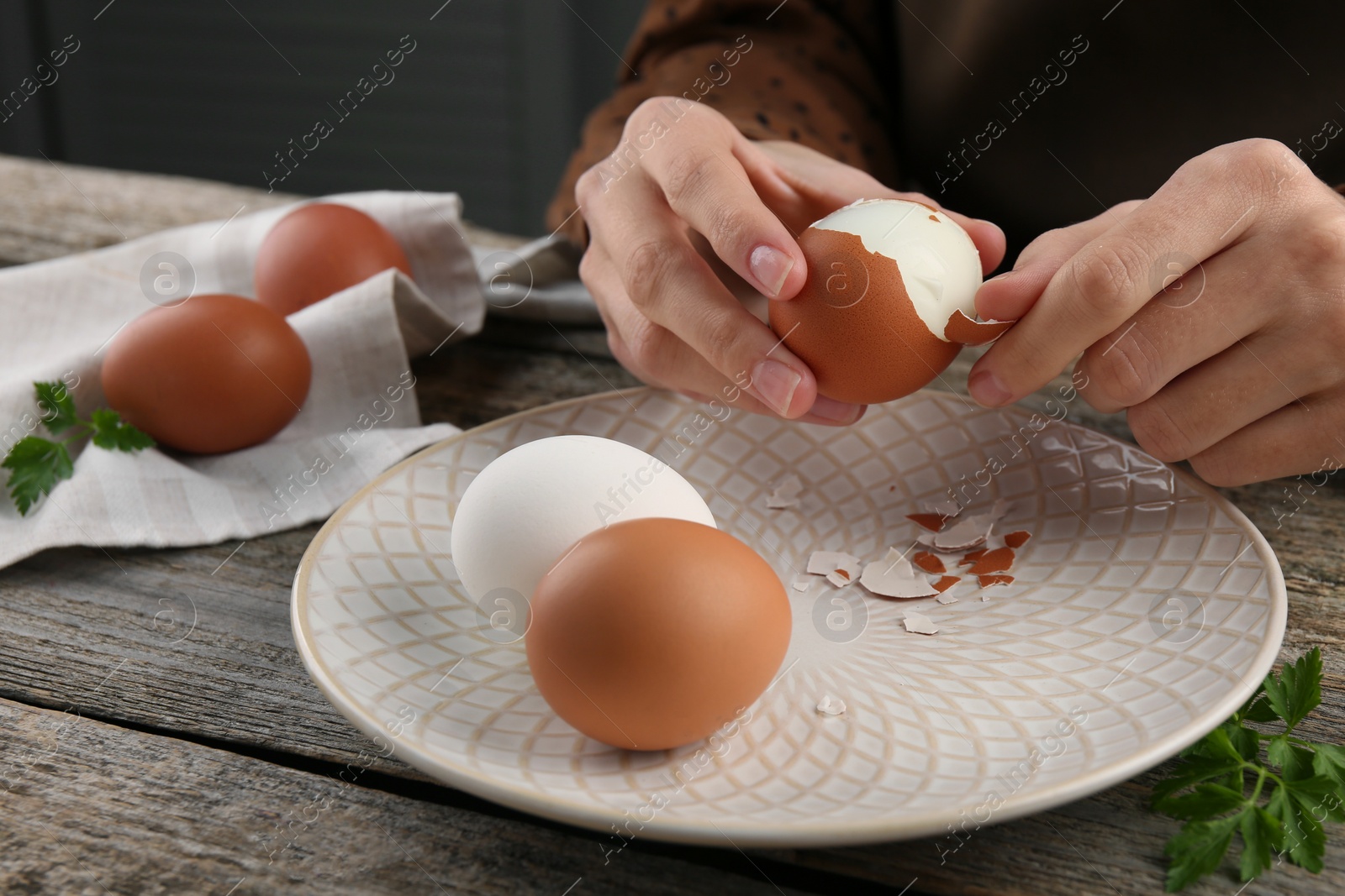 Photo of Woman peeling boiled egg at old wooden table, closeup