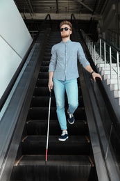 Photo of Blind person with long cane on escalator indoors