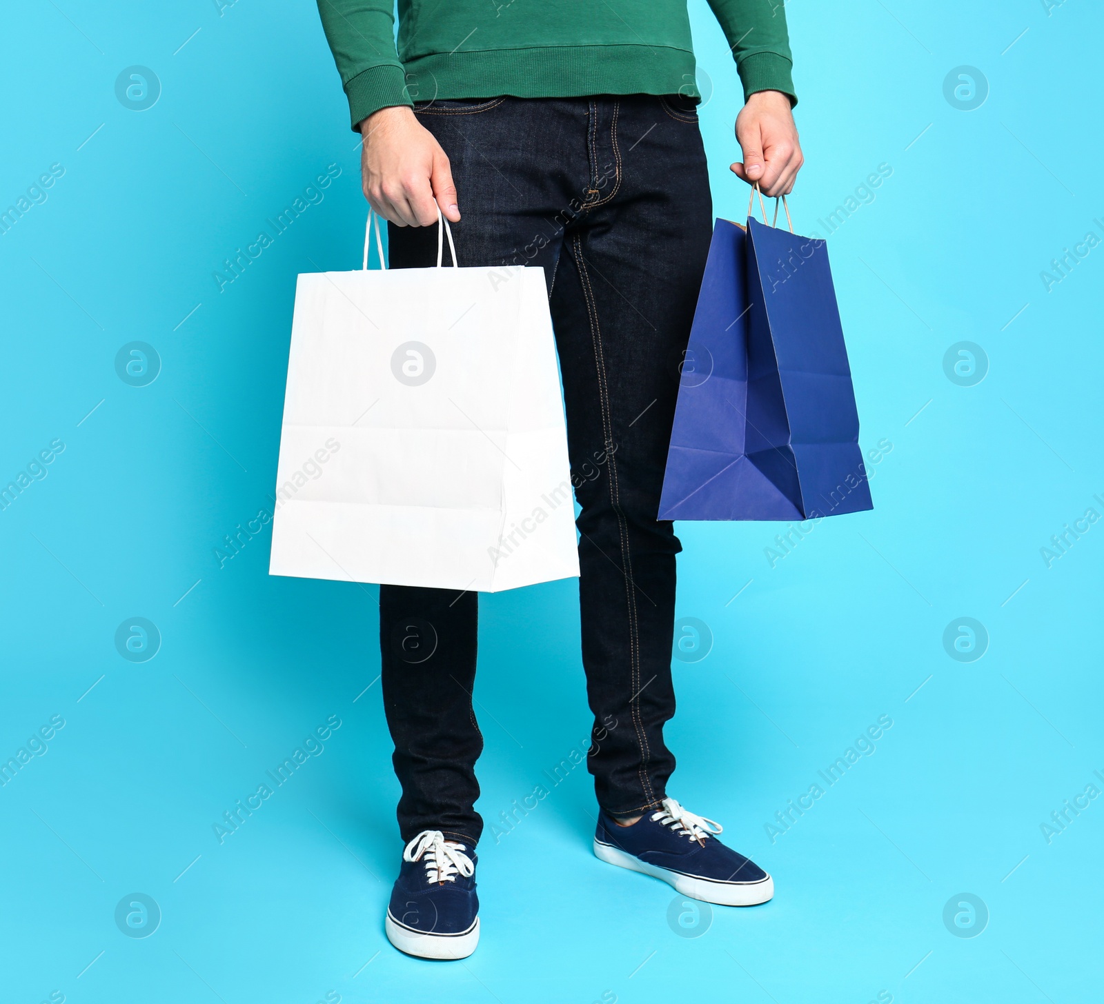 Photo of Young man with paper bags on blue background, closeup