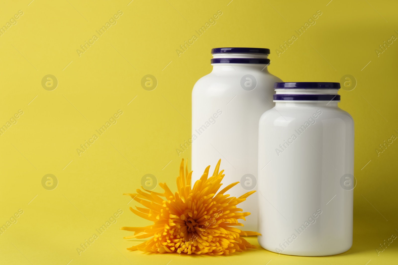 Photo of Medicine bottles near flower on yellow background, space for text