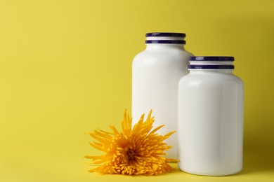 Medicine bottles near flower on yellow background, space for text