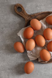 Photo of Chicken eggs, wooden board and parchment paper on grey table, flat lay