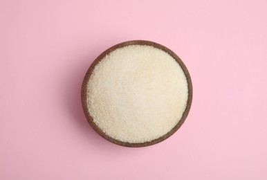 Photo of Gelatin powder in wooden bowl on pink background, top view
