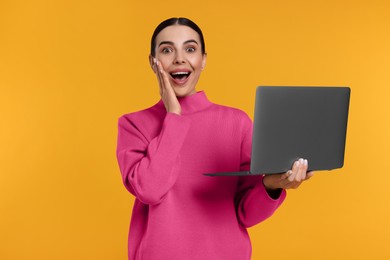 Emotional woman with laptop on orange background
