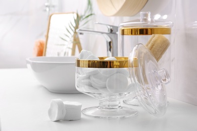 Photo of Glass jars with cotton pads and loofahs on table in bathroom