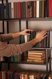 Photo of Young man choosing book on shelf in home library, closeup