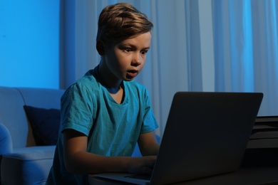 Shocked little child with laptop in dark room. Danger of internet