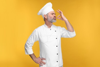 Photo of Chef in uniform showing perfect sign on orange background