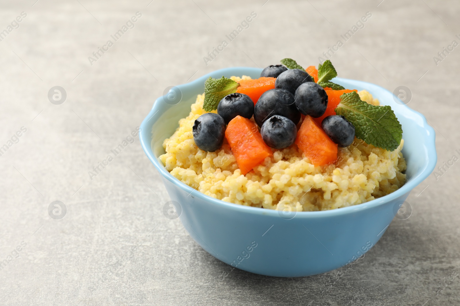 Photo of Tasty millet porridge with blueberries, pumpkin and mint in bowl on light grey table, closeup. Space for text