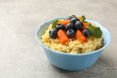 Tasty millet porridge with blueberries, pumpkin and mint in bowl on light grey table, closeup. Space for text