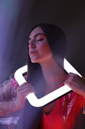 Photo of Fashionable portrait of beautiful woman wearing transparent coat with square lamp on dark background in neon lights