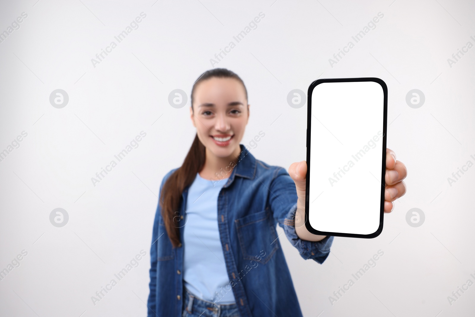Photo of Young woman showing smartphone in hand on white background, selective focus. Mockup for design