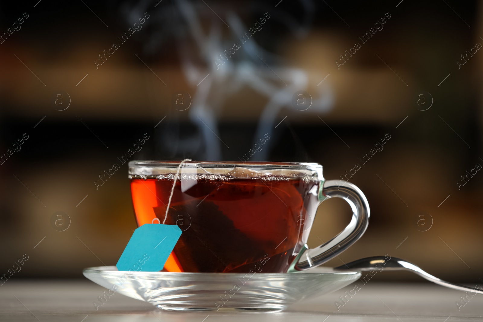 Photo of Tea bag in glass cup of hot water on table against blurred background