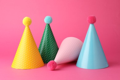 Photo of Beautiful party hats with pompoms on pink background