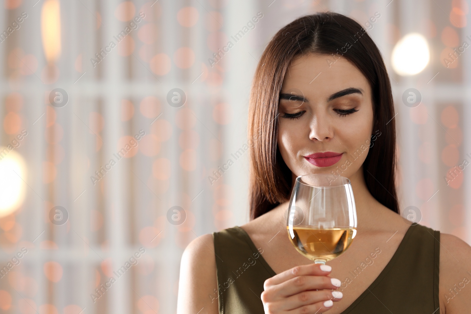 Photo of Beautiful young woman with glass of luxury white wine indoors. Space for text