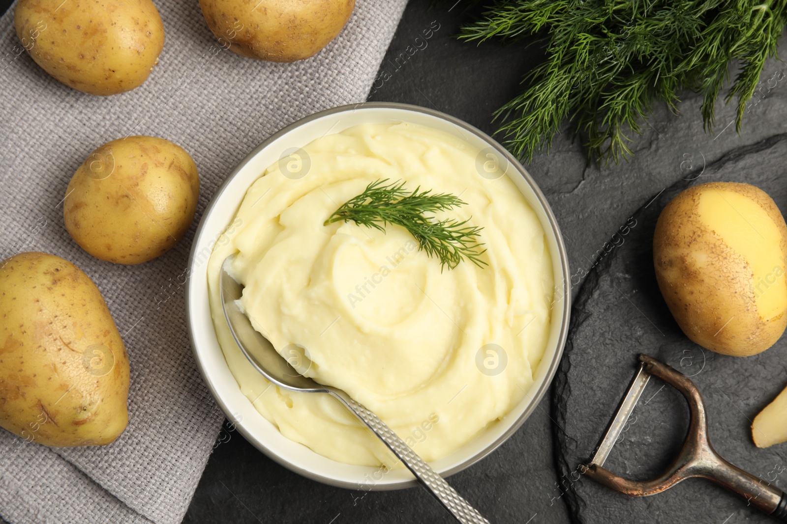 Photo of Freshly cooked homemade mashed potatoes and raw ingredients on black table, flat lay