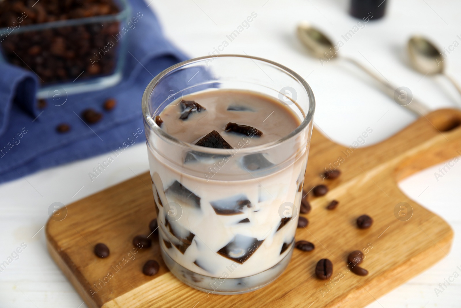 Photo of Glass of milk with grass jelly and coffee beans on white table, closeup