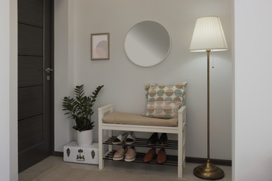 Photo of Stylish hallway room interior with bench, shoes and round mirror