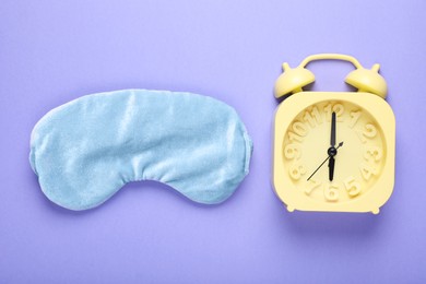 Soft sleep mask and alarm clock on purple background, flat lay