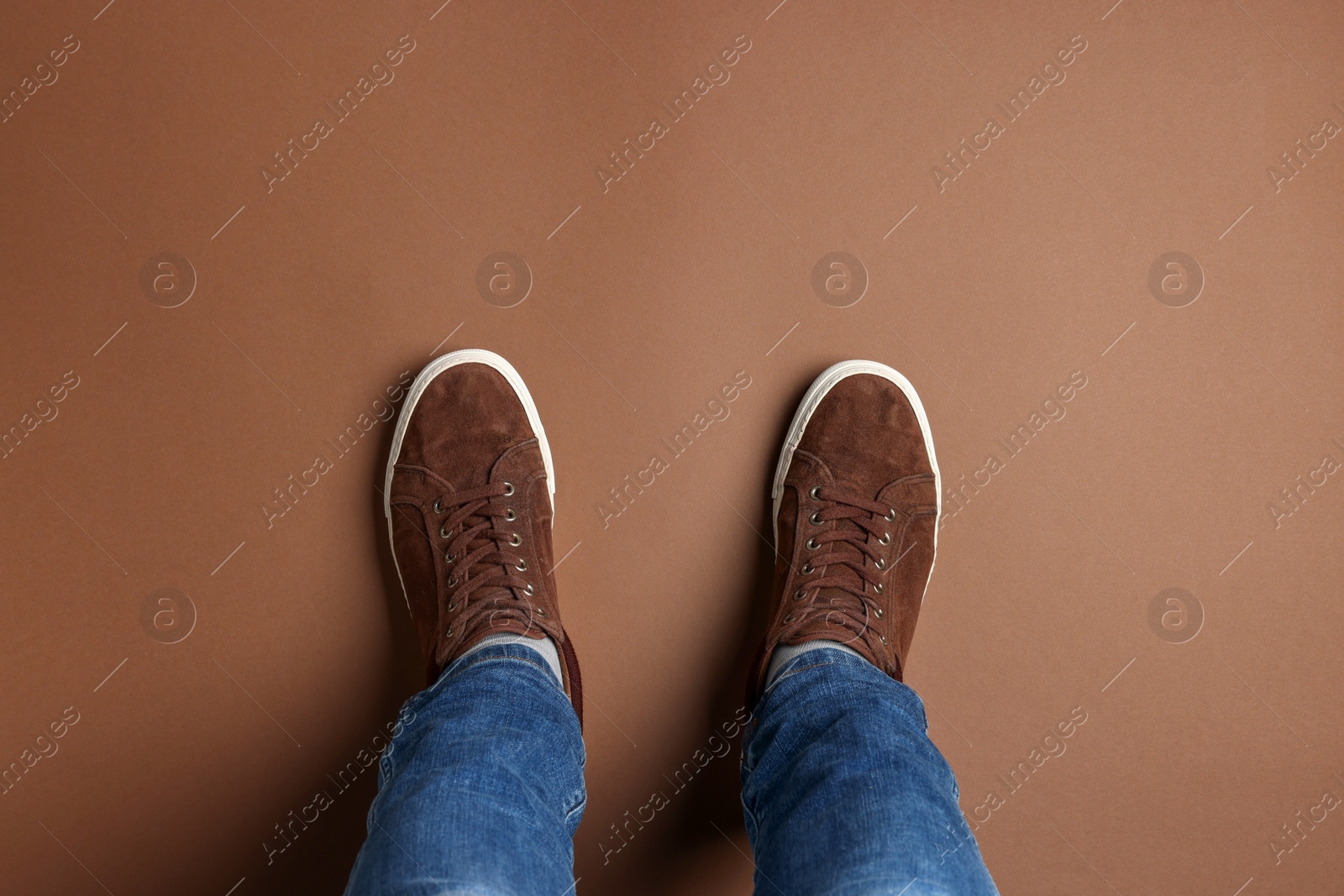 Photo of Man in stylish sneakers standing on brown background, top view