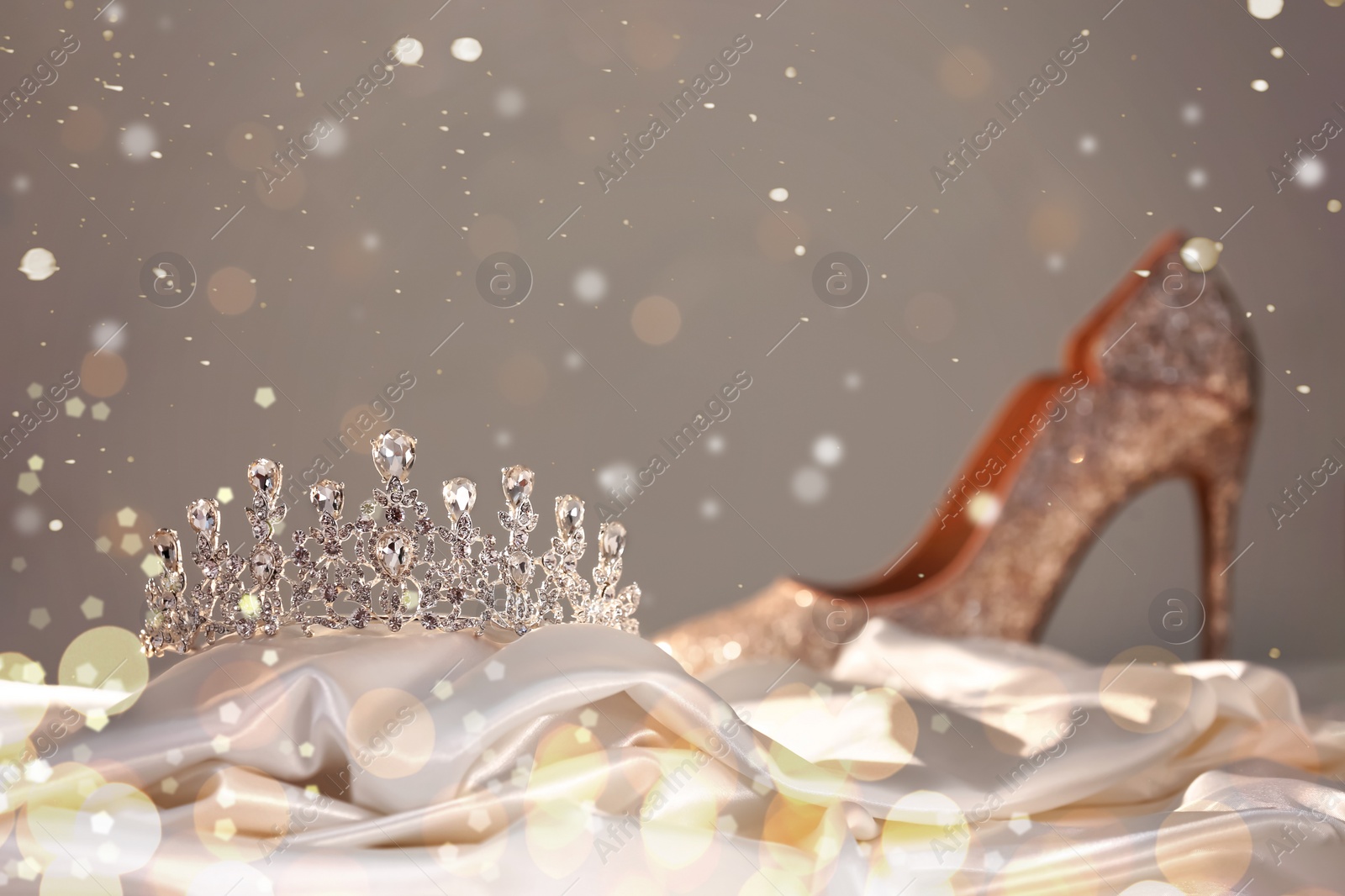 Image of Beautiful silver tiara with diamonds on white silk near high heel shoe. Bokeh effect