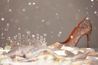 Beautiful silver tiara with diamonds on white silk near high heel shoe. Bokeh effect