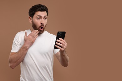Photo of Surprised man with smartphone on light brown background. Space for text