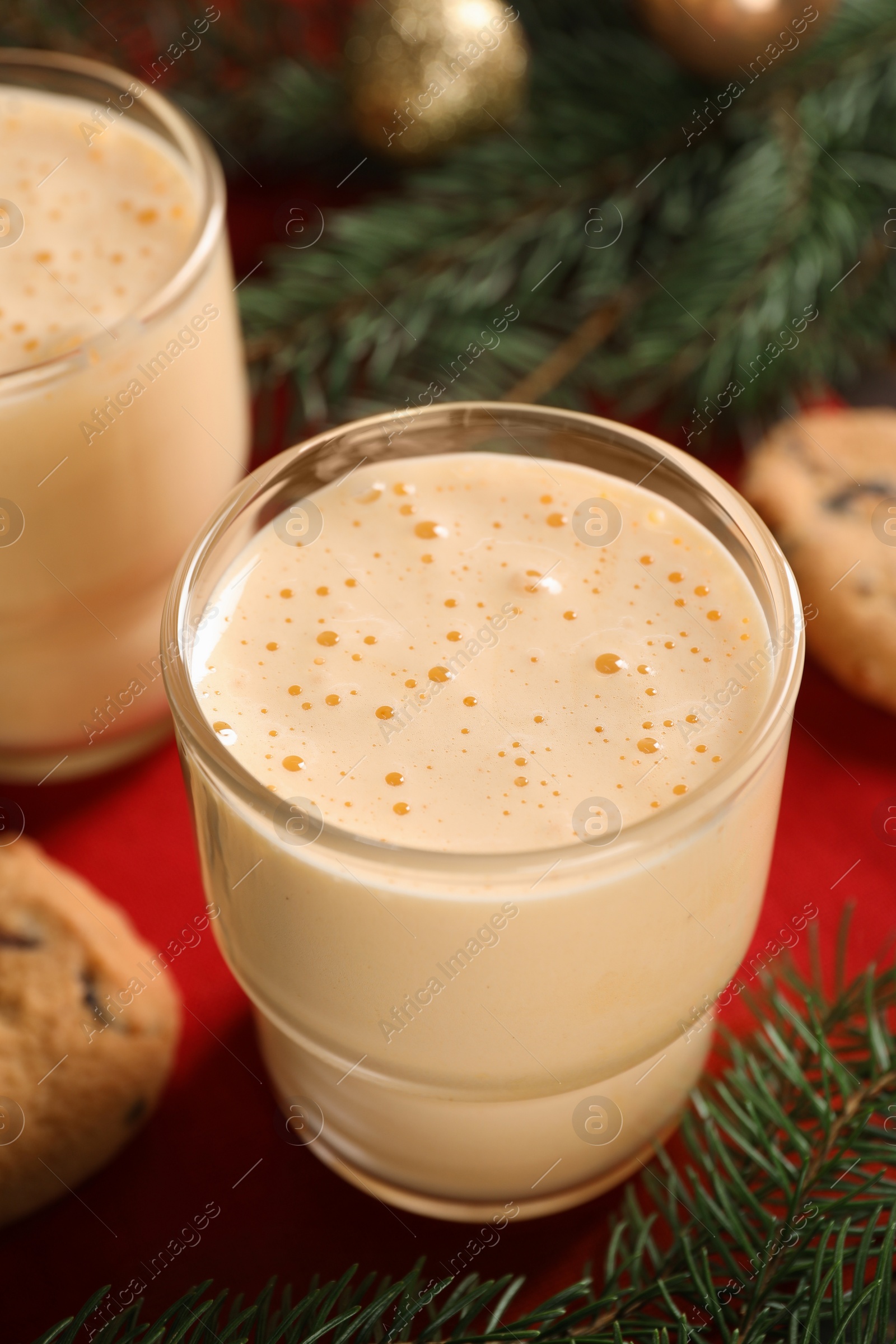 Photo of Tasty eggnog, cookies and fir branches on red cloth, closeup