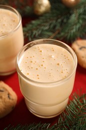 Photo of Tasty eggnog, cookies and fir branches on red cloth, closeup