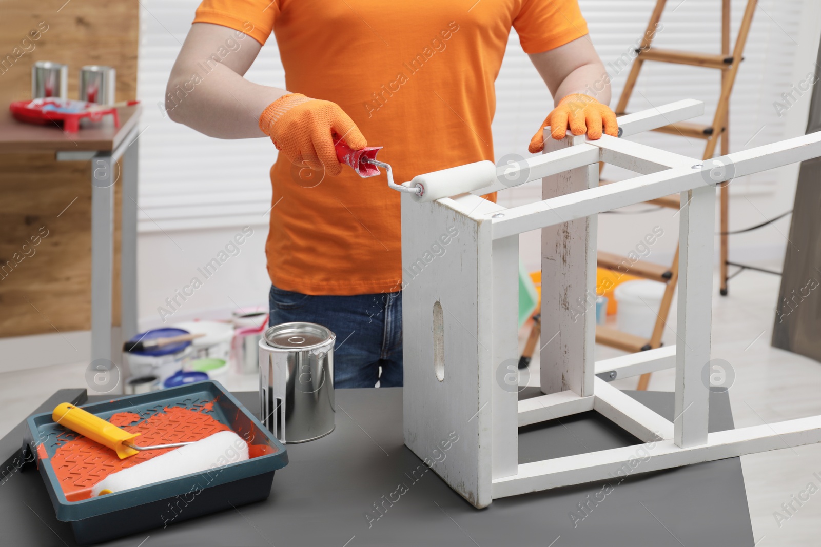 Photo of Man using roller to paint bekvam with white dye at black wooden indoors, closeup