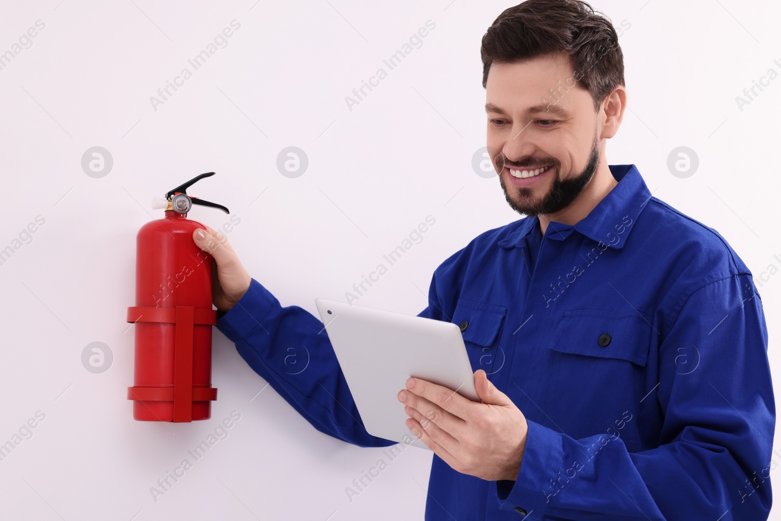 Photo of Man with tablet checking fire extinguisher indoors