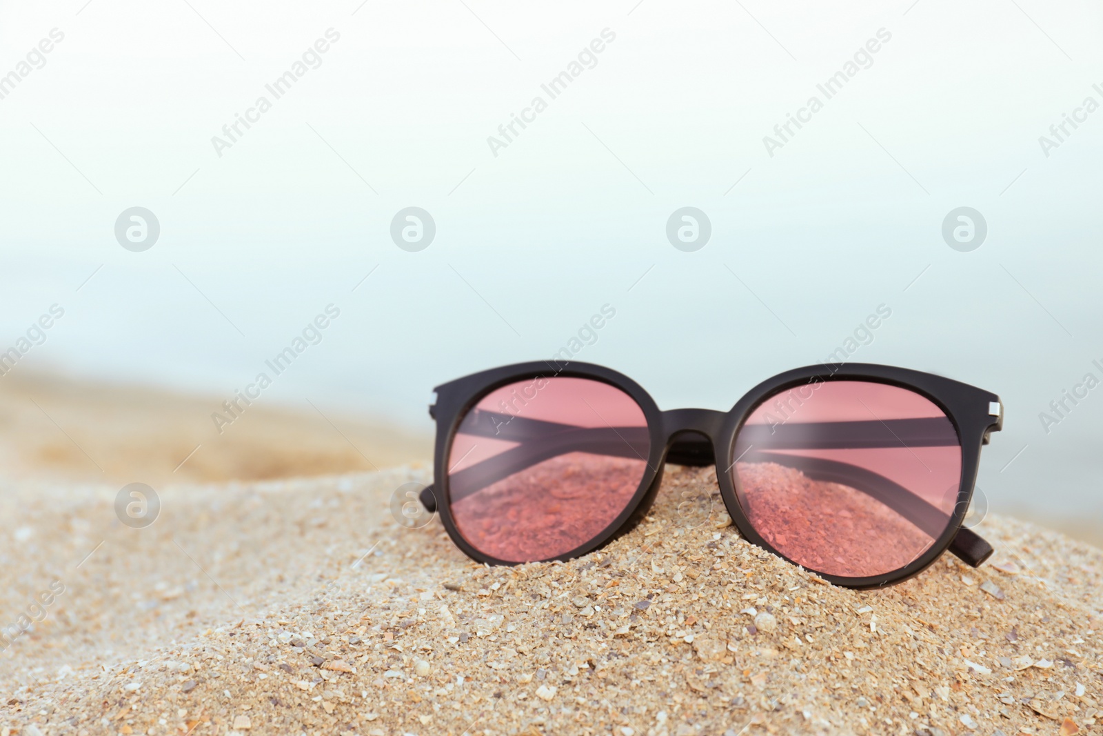 Photo of Stylish sunglasses on sandy beach near sea