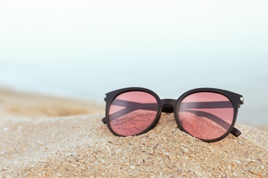 Stylish sunglasses on sandy beach near sea