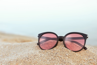 Photo of Stylish sunglasses on sandy beach near sea