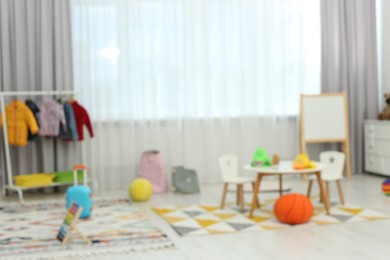 Blurred view of child`s playroom with different toys and furniture. Stylish kindergarten interior